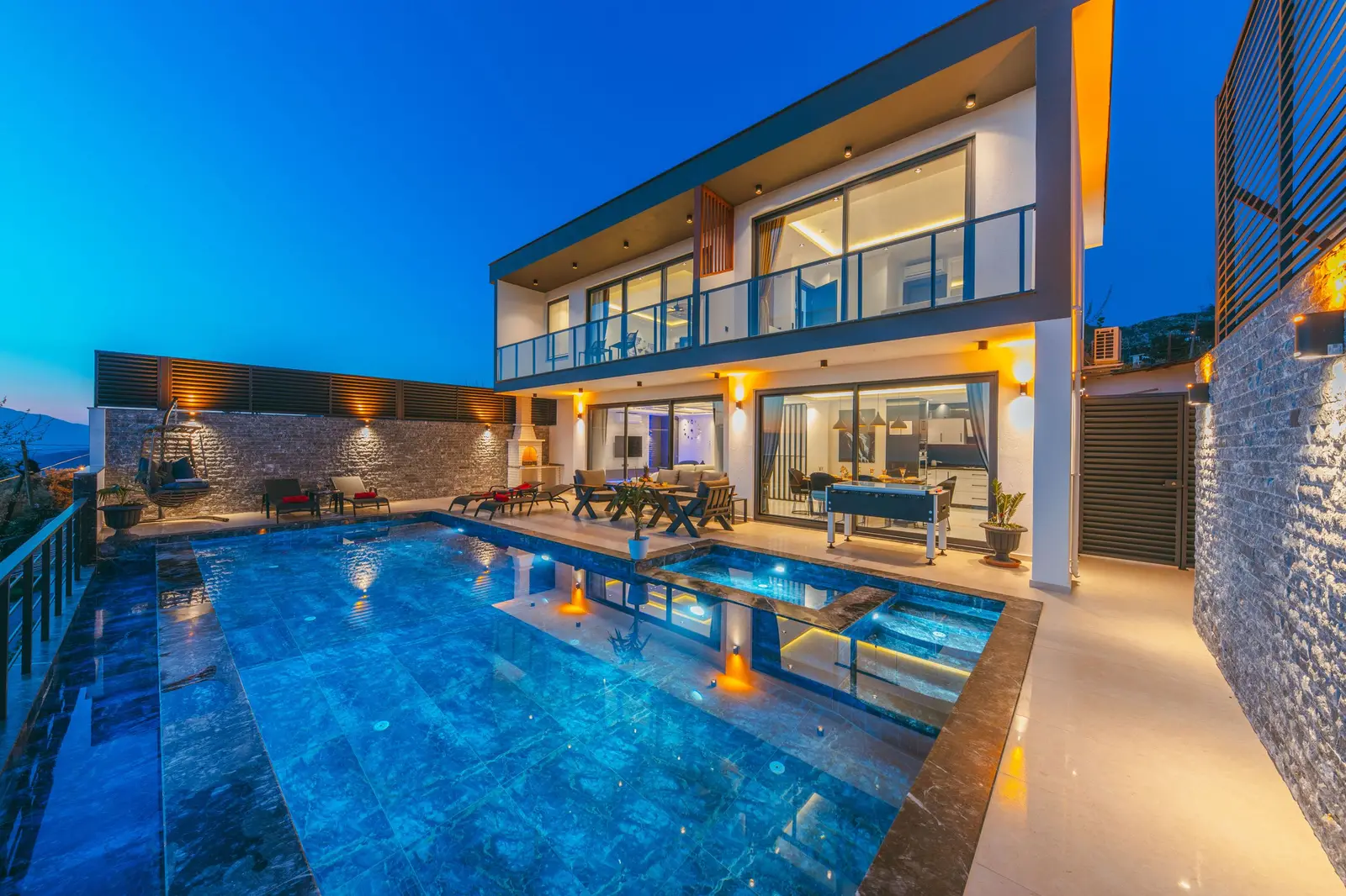A modern home at dusk with its pool and terraces lit